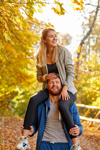 couple enjoy the walk in the forest, adorable young female in sportswear sit on the neck of boyfriend or husband, have fun, in contemplation of nature