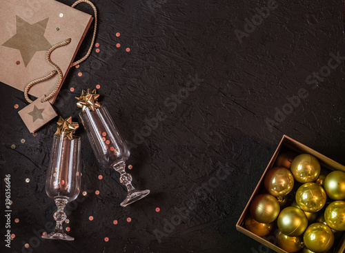 Wine glasses, gift bag, Christmas balls in a box, gold sparkles, gift bag on a black background. Christmas composition..Place for signature.