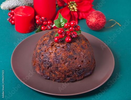 Traditional Christmas pudding with holly on top and Christmas decoration on the background