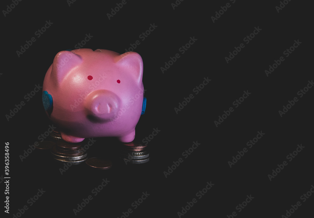 A pink piggy bank stands on coins. Dark background