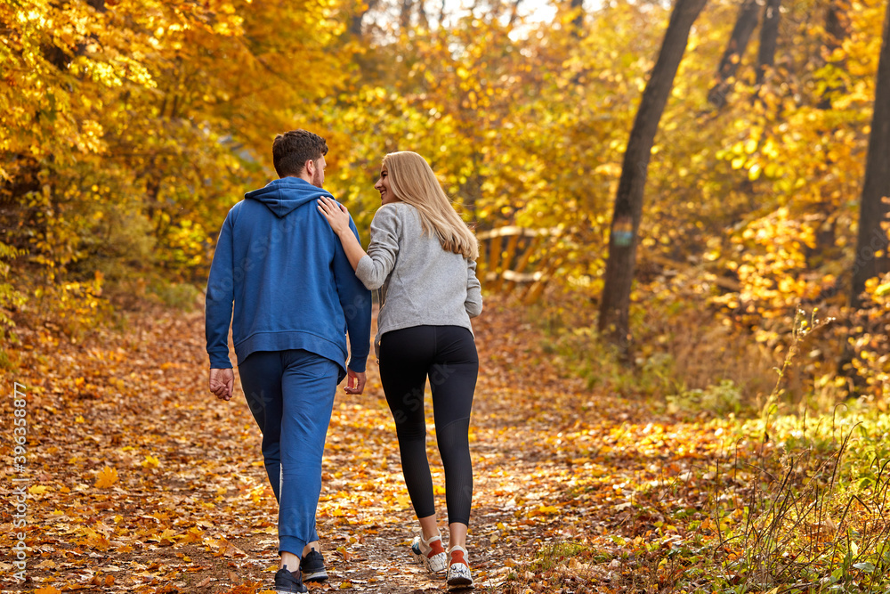Obraz premium rear view on couple enjoying jogging on a country road through the beautiful autumn forest, exercise and fitness concept