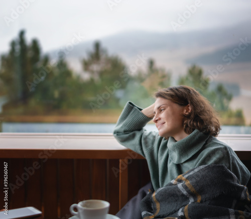 Leinwand Poster Young happy woman in green sweater by the window in a country house chalet with