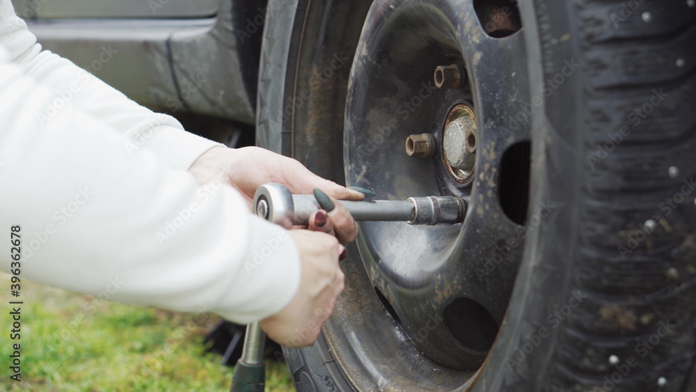 A girl with a manicure changes a car wheel, jack, wrench, grease.