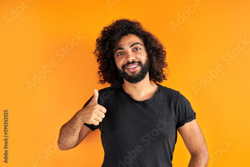 portrait of an excited bearded arab man standing isolated over yellow background, good job. he shows thumbs up at camera