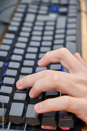  Close-up addiction guy with manly hands playing video game on computer screen with fingers on keyboard 