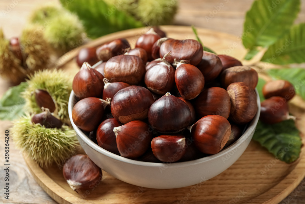 Fresh sweet edible chestnuts in bowl on wooden board Fresh sweet edible chestnuts in bowl on wooden board