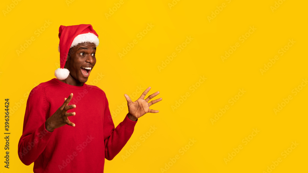 Shocking Offer. Amazed African Guy In Santa Hat Looking At Copy Space Shocking Offer. Amazed African Guy In Santa Hat Looking At Copy Space