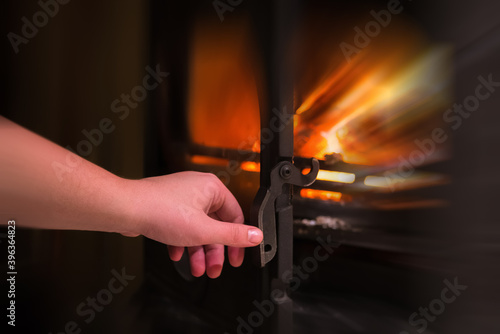 Human hand opening a door of the burning fireplace with wooden l