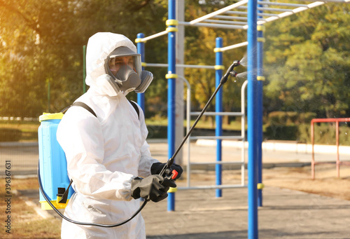 Man in hazmat suit spraying disinfectant around outdoor gym. Surface treatment during coronavirus pandemic