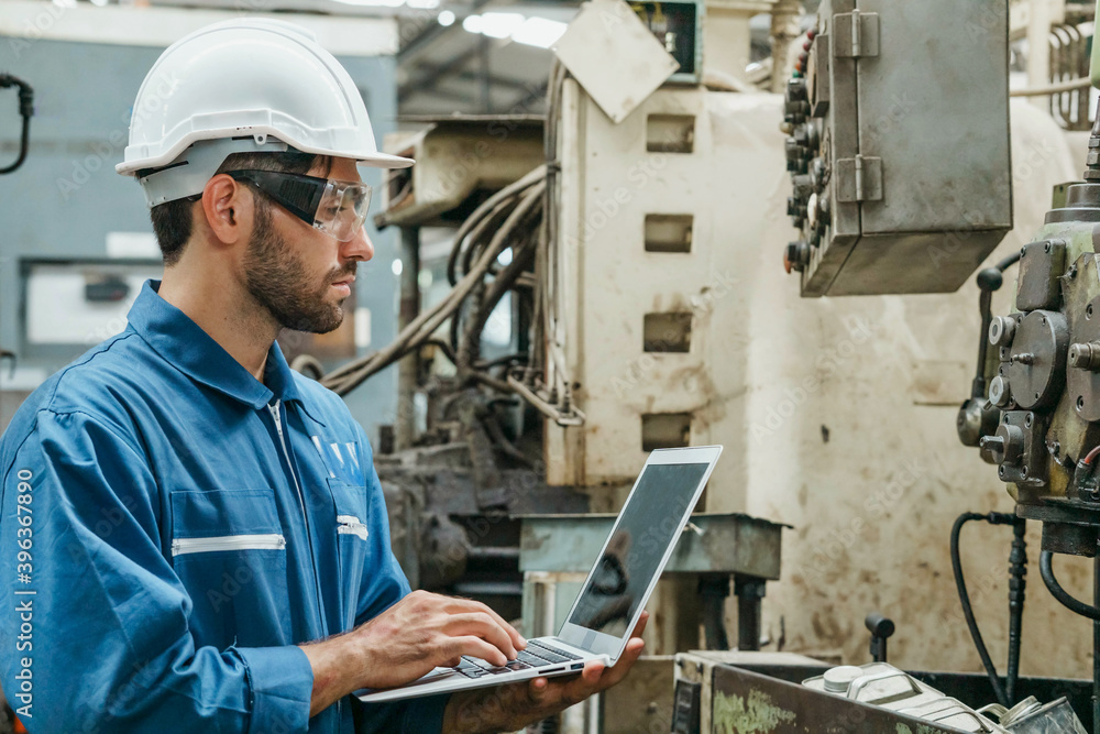 Factory Engineer or mechanical worker wearing white safety helmet holding laptop and checking on production in a factory. Industrial,Warehouse Heavy Mechanic, Engineering Concept. Factory Engineer or mechanical worker wearing white safety helmet holding laptop and checking on production in a factory. Industrial,Warehouse Heavy Mechanic, Engineering Concept.