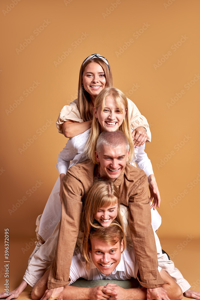 portrait of happy group of caucasian youth having fun in studio with brown background, beautiful people in trendy wear are cheerful. models, people, emotions concept