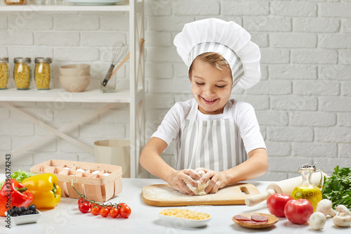 little child boy in cap and an apron playing with dough in the kitchen