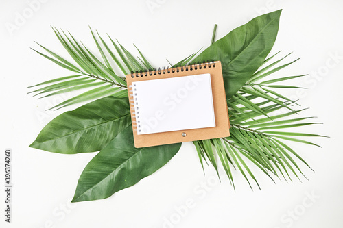 White blank note paper and big green tropical leaves on background. Flat lay. Top view. Copy space.