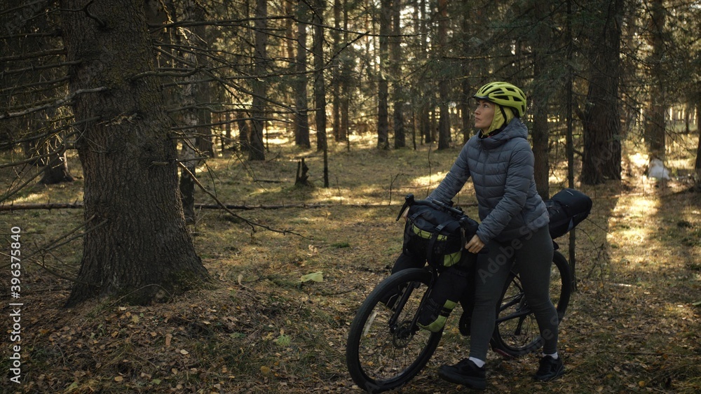 Naklejka premium The woman travel on mixed terrain cycle touring with bike bikepacking. The traveler journey with bicycle bags. Magic forest park.