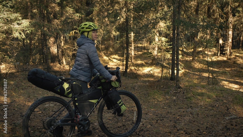 Naklejka premium The woman travel on mixed terrain cycle touring with bike bikepacking. The traveler journey with bicycle bags. Magic forest park.