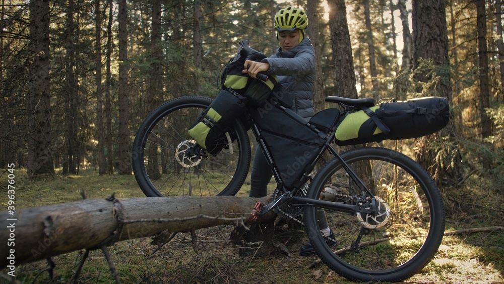 Fototapeta premium The woman travel on mixed terrain cycle touring with bike bikepacking. The traveler journey with bicycle bags. Magic forest park.