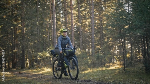 The woman travel on mixed terrain cycle touring with bike bikepacking. The traveler journey with bicycle bags. Magic forest park.