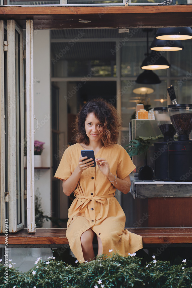 Young woman wearing yellow dress using her smart phone in a coffee shop terrace
