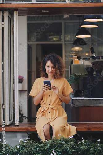 Obraz na płótnie Young woman wearing yellow dress using her smart phone in a coffee shop terrace w salonie