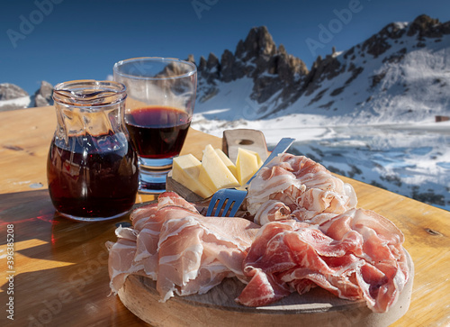 plate of cold cuts and mountain cheeses in a wooden tray - carafe of red wine and glass
