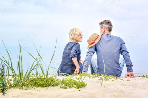 happy man and woman sitting on the sand near the sea