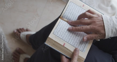 Modern muslim man reading Quran book indoors at home