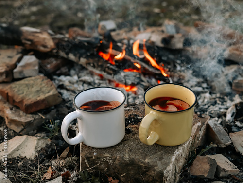 Two metal mugs with mulled wine stand near the fire. Autumn picnic.