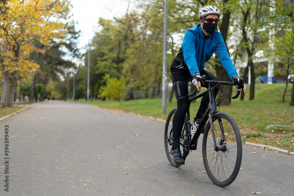 A young man in a protective mask and helmet rides a bicycle on the road. Active rest in quarantine. Fighting excess weight. A young man in a protective mask and helmet rides a bicycle on the road. Active rest in quarantine. Fighting excess weight.