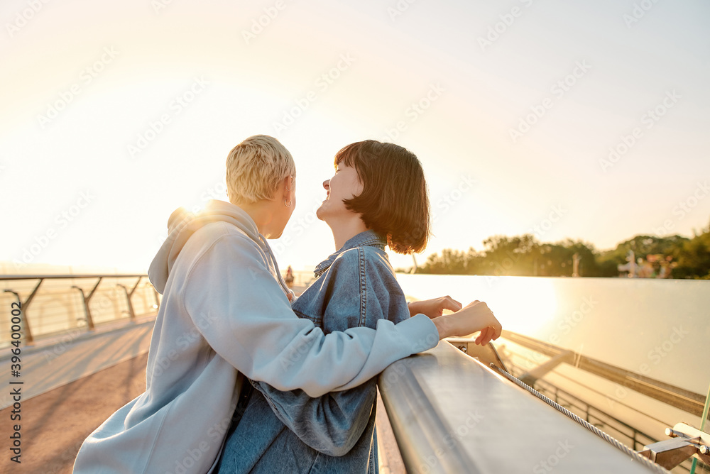 Fun time together. Lesbian couple laughing, standing together, leaning on the bridge and watching the sunrise. Homosexuality, LGBT and love concept