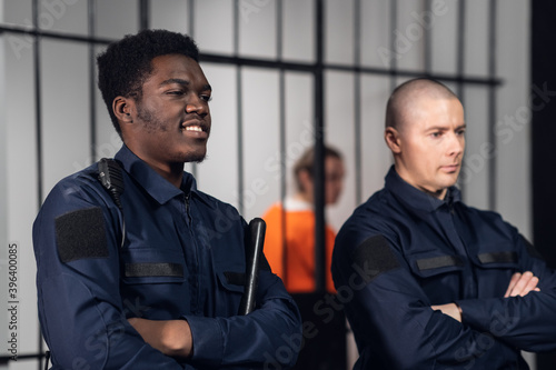 Black and white prison guards stand with batons in the background of cells with prisoners criminals photo