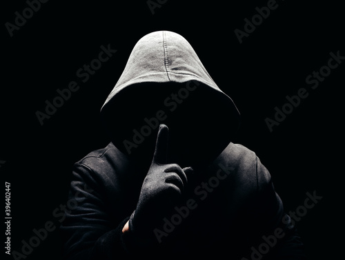 Photo of a scary horror man in hoodie showing silence hand sign in dark. photo