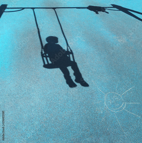 Shadow of a little boy on a swing at playground with blue cover on a ground