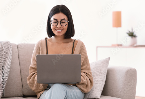 Asian woman sitting on couch and working on laptop pc