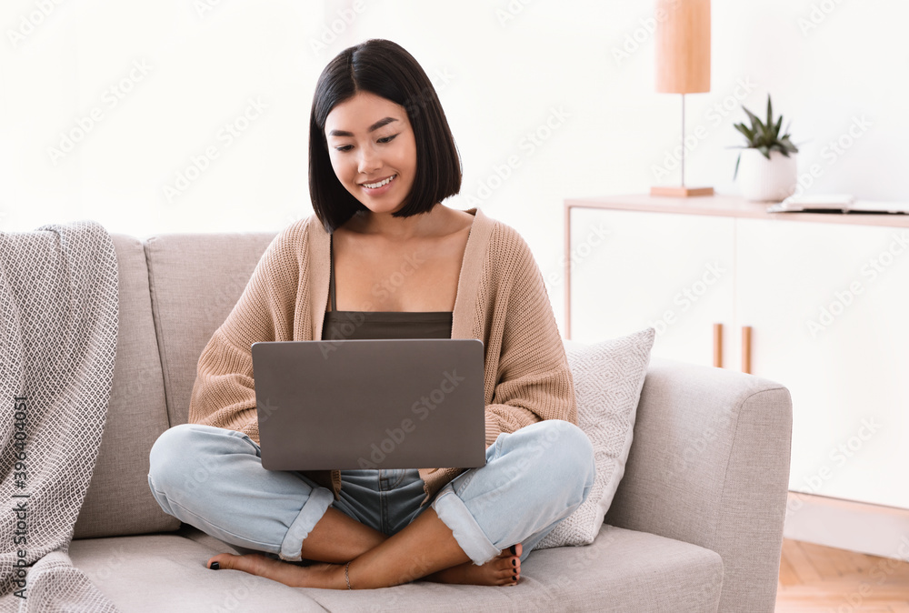 Asian woman sitting on couch and working on laptop Asian woman sitting on couch and working on laptop