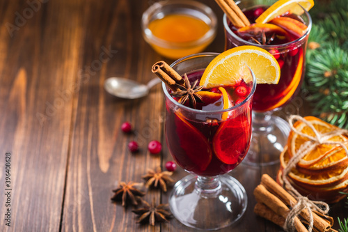 Hot wine drink with spices and fruits in a tall glass and branches of a Christmas tree on a wooden background, copy space. Christmas mulled wine or punch.
