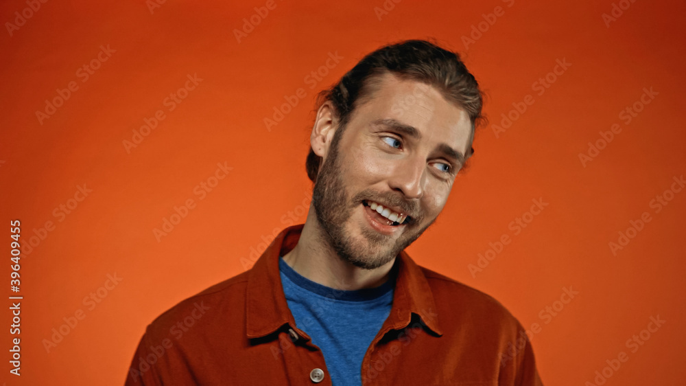joyful and bearded man smiling while looking away on orange joyful and bearded man smiling while looking away on orange