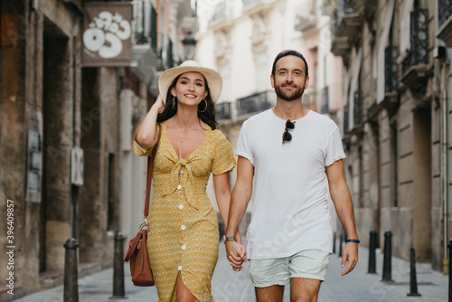 A girl in a yellow dress with a plunging neckline and her boyfriend with a beard are walking in old Spain town. A couple of tourists on a date in the evening Valencia. A lady is checking her hat. © Roman Tyukin