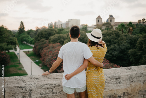 A girl in a yellow dress and a hat and her boyfriend is hugging each other on the ancient bridge in old Spain town. A couple of tourists is enjoying the view of the park in the evening in Valencia. photo