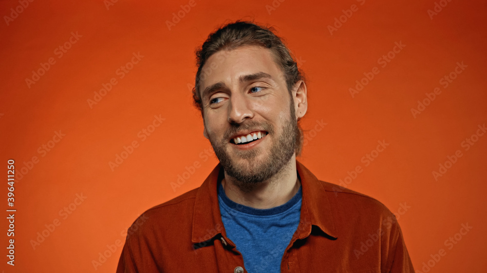 Fototapeta premium pleased and bearded man smiling while looking away on orange