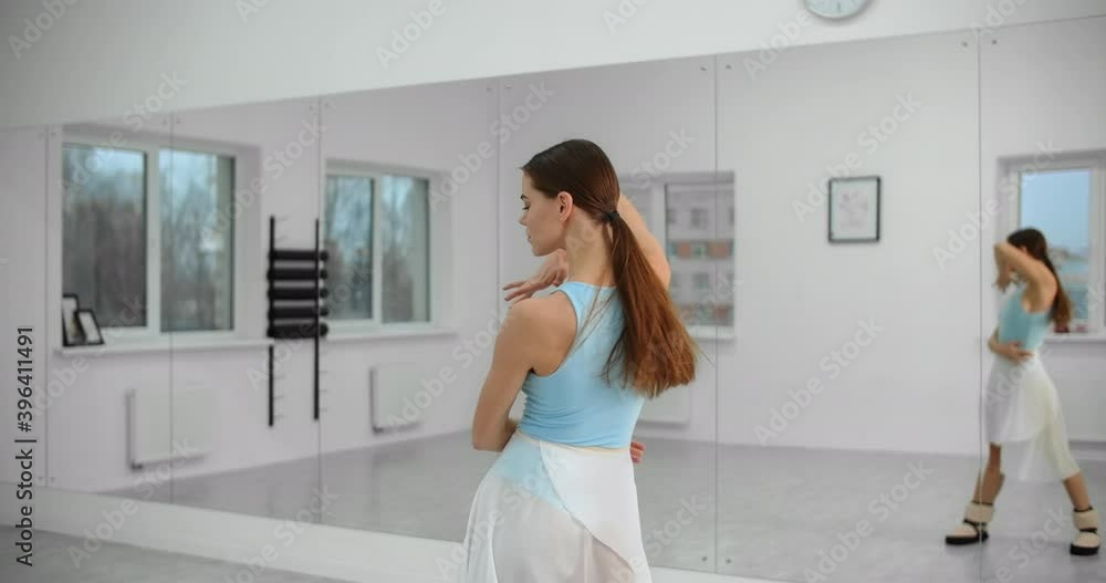 Dancer warms up infromt of the mirror wall in the white bright dance hall before rehearsal, ballet rehearsal, ballerina in the ballet studio, dance hall lesson, 4k 60p Prores HQ Dancer warms up infromt of the mirror wall in the white bright dance hall before rehearsal, ballet rehearsal, ballerina in the ballet studio, dance hall lesson, 4k 60p Prores HQ