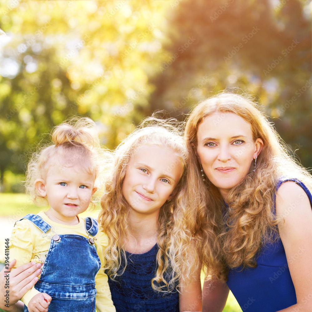Fototapeta premium Mother and little daughters. Happy family portrait. Mom hug. Outdoor lifestyle. Cute face. Smile positive parent. Female child love. Green background. Baby girl. Casual cloth
