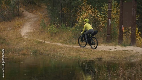 The woman travel on mixed terrain cycle touring with bikepacking. The traveler journey with bicycle bags. Sportswear in green black colors. The trip in magical autumn forest, river stream. photo