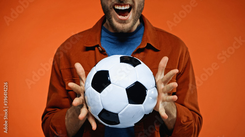 cropped view of excited man holding soccer ball on orange