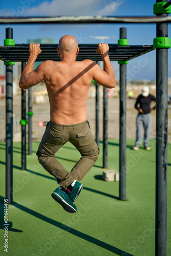 Photo of muscular man doing pull ups on horizontal gymnastic bar © JENOCHE