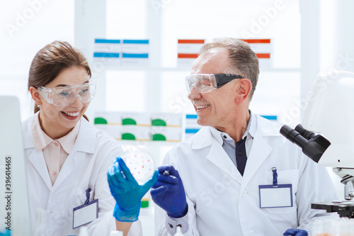 smiling scientists with a Petri dish sitting at a laboratory table.