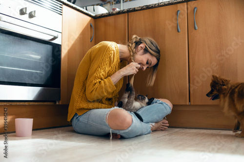 Beautiful young woman playing with her cute lovely animals sitting on the floor in the kitchen at home. photo