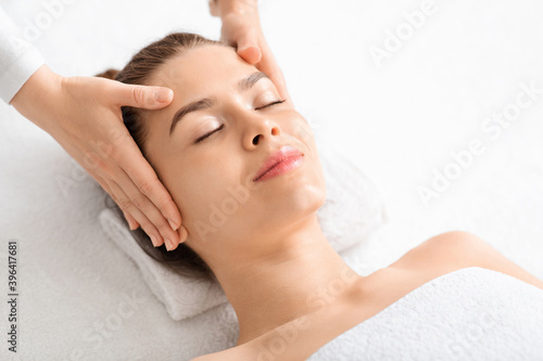 Joyful young woman relaxing during face lifting massage, copy space
