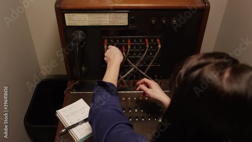 Stressed out woman operator switching tangled telephone switchboard cables photo
