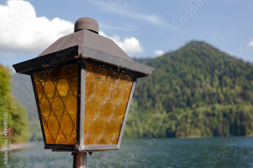 Street old vintage square-shaped lantern with brown glass against the backdrop of green mountains and blue sky with clouds, used as a background or texture