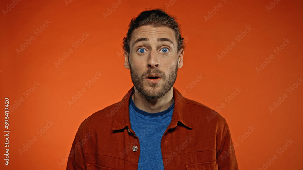shocked bearded man in shirt looking at camera on orange